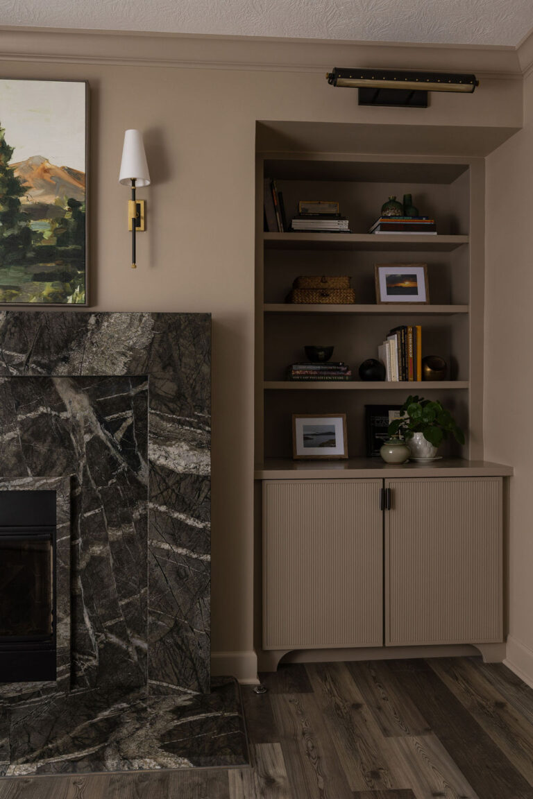 Dark marble fireplace beside open wood shelving styled with framed art and books.