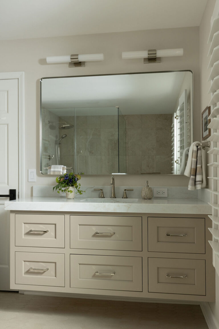 Double vanity with taupe cabinetry, brass hardware, and a wide arched mirror.