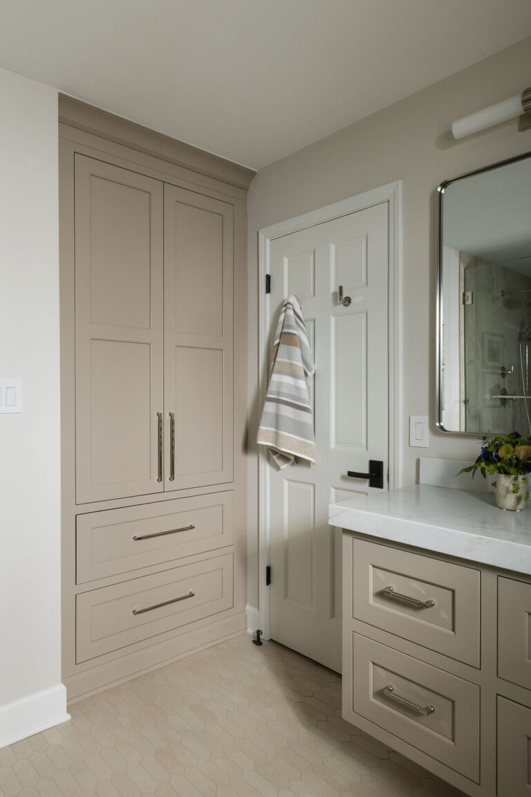 Bathroom cabinetry wall with tall storage units and a glimpse into an adjoining tiled shower.