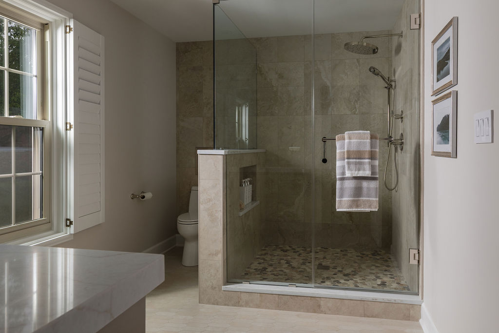 Glass-enclosed walk-in shower with pebble tile flooring, brass fixtures, and a striped towel hanging inside.