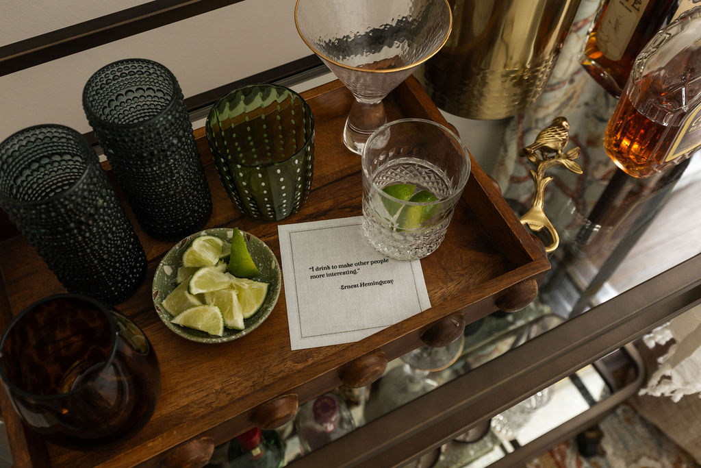 Bar tray styled with cut crystal glassware, limes, a small potted cactus, and a handwritten cocktail card.
