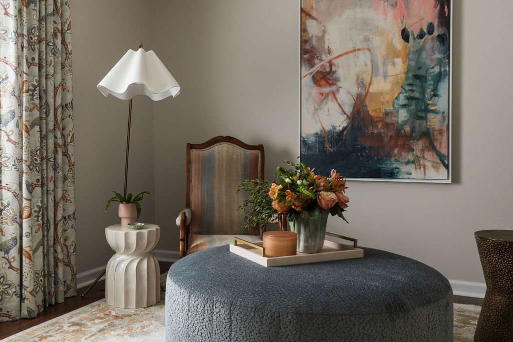 Cozy reading corner with a wingback chair, scalloped side table, and a fresh floral arrangement on a round blue ottoman.